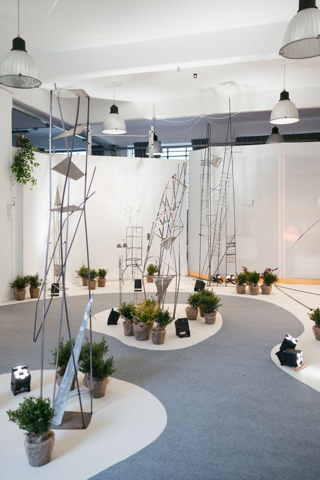 Allestimento di Connessioni: sculture in ferro e piante in vaso su un percorso bianco