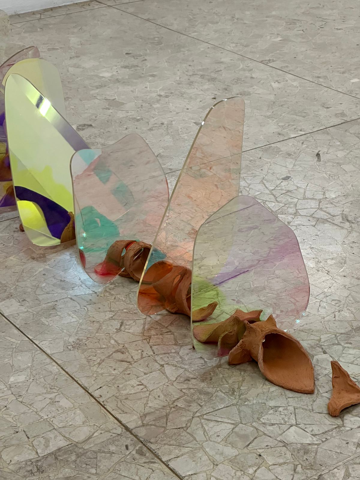 Sculture in plexiglas iridescente e terracotta sul pavimento della galleria