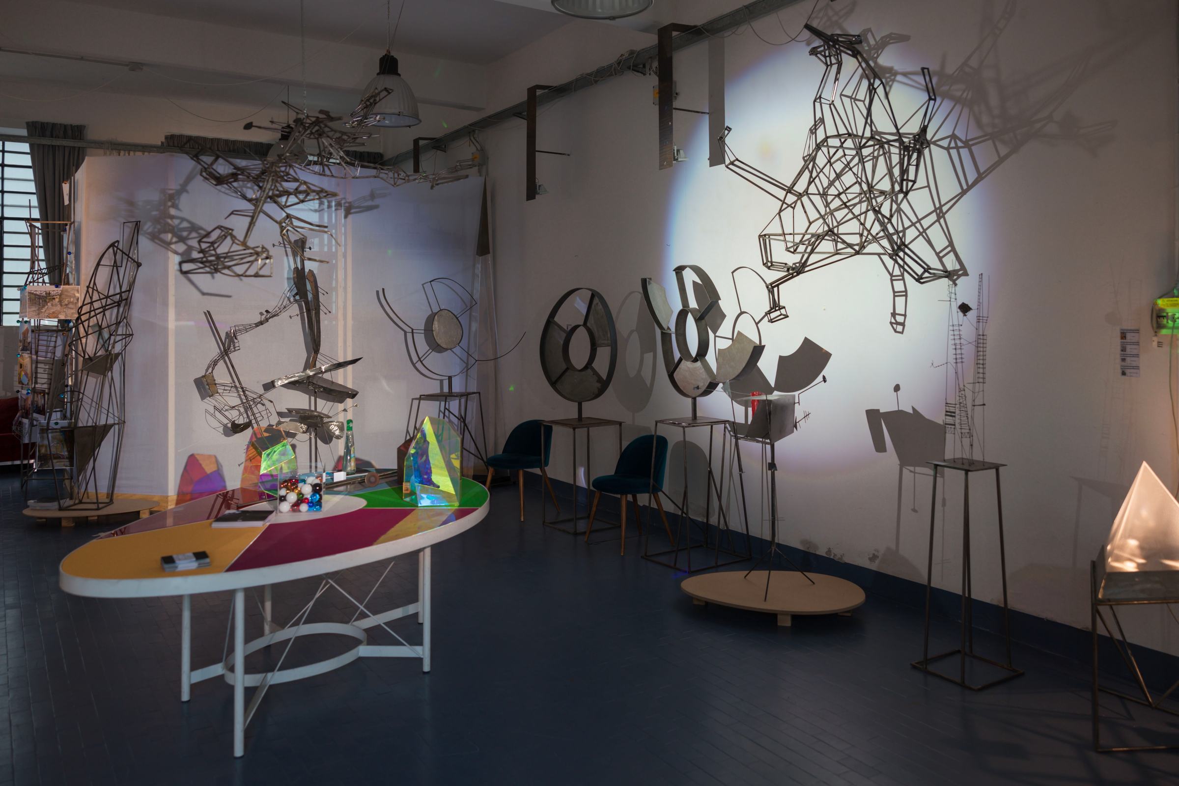 Interno di Spazio Pirotecnico con sculture in ferro alle pareti e opere in plexiglas colorato su un tavolo