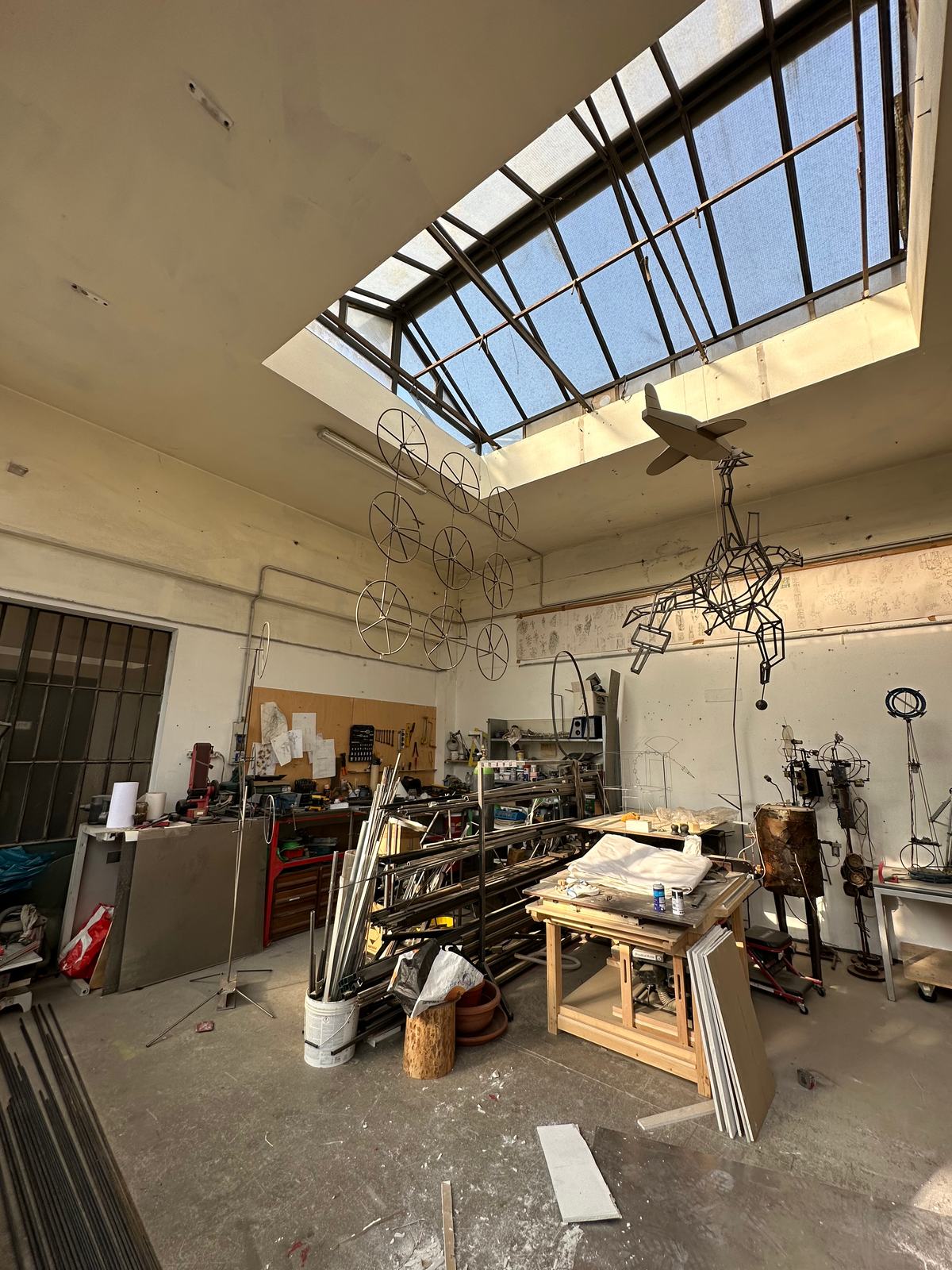 Il laboratorio con lucernario, banchi da lavoro e sculture in ferro appese al soffitto