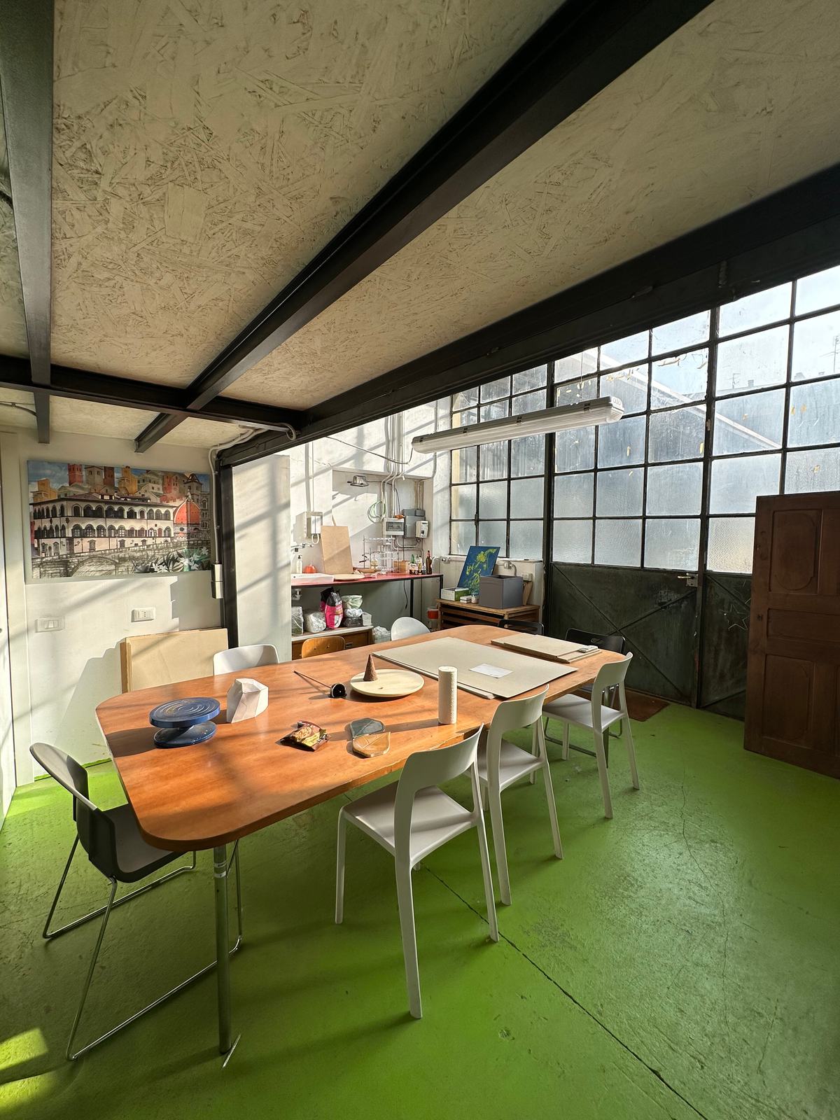 Sala con un lungo tavolo, sedie bianche e pavimento verde, usata per i laboratori